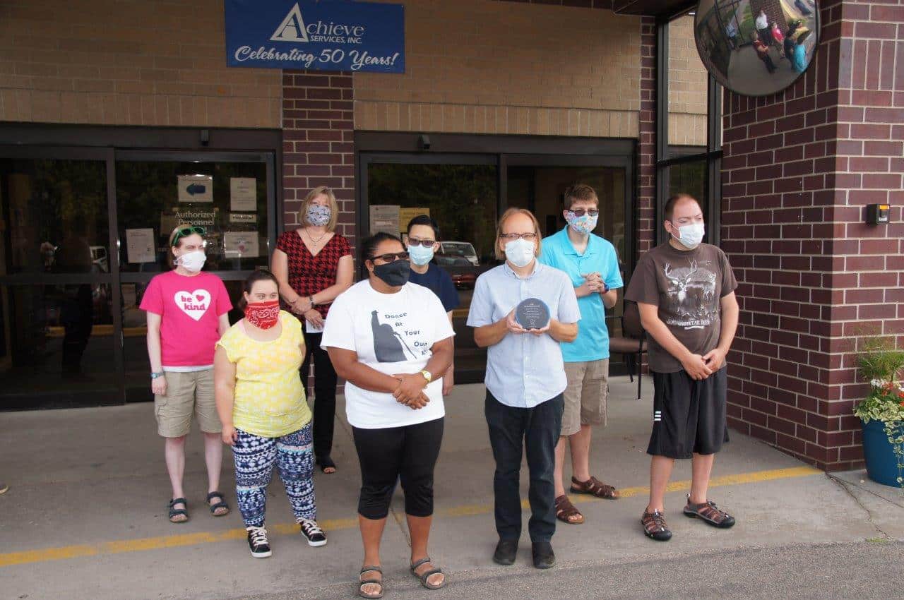 Members of Dance At Your Own Risk stand outside Acheive's entrance with MOHR President and Training Specialist Joe Loskota who is holding the award in his hands