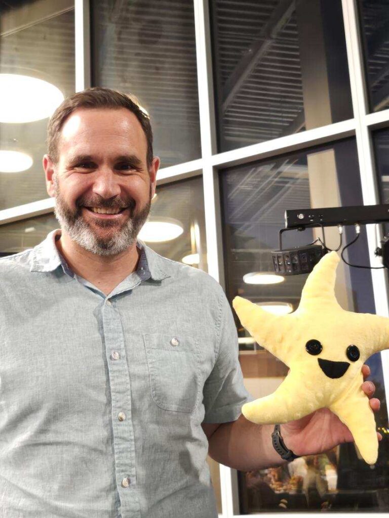 Staff member named Ben Seeling holding a plush starfish award